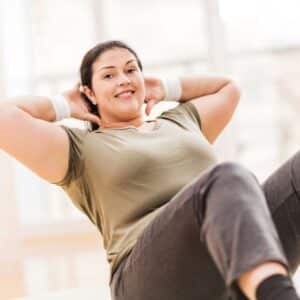 Smiling overweight mid adult woman doing sit ups and looking at the camera.