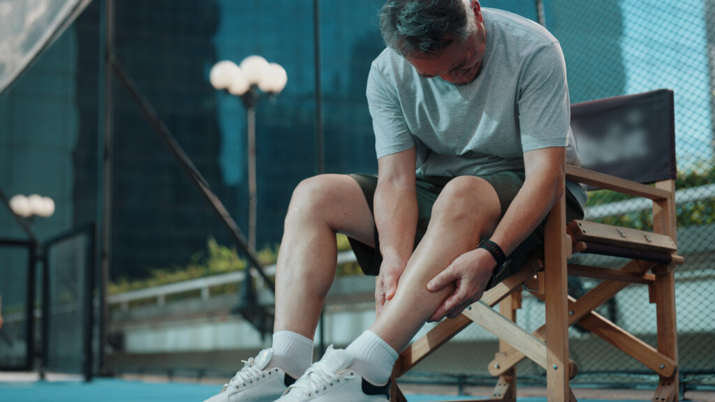 Man seated outdoors holding his lower leg, illustrating leg pain that may be associated with peripheral artery disease (PAD).